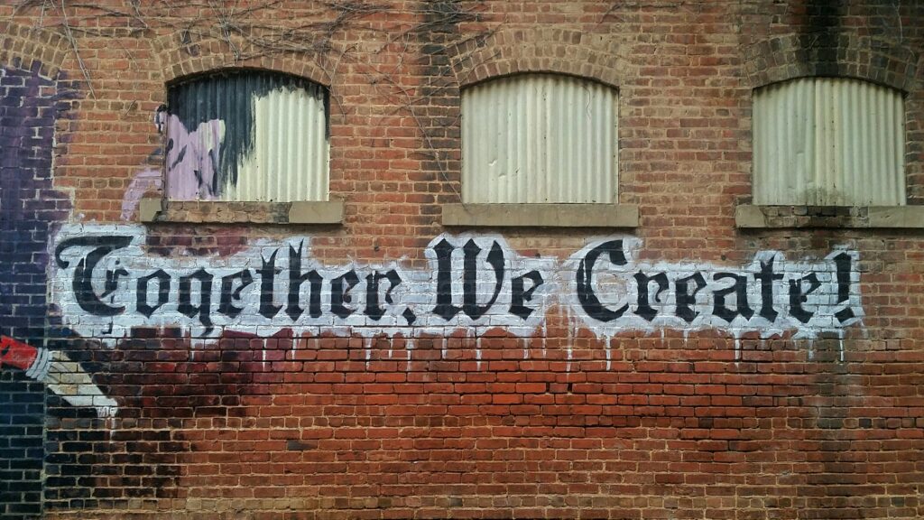 Red brick wall with graffiti letters written to remind us that "Together We Create"